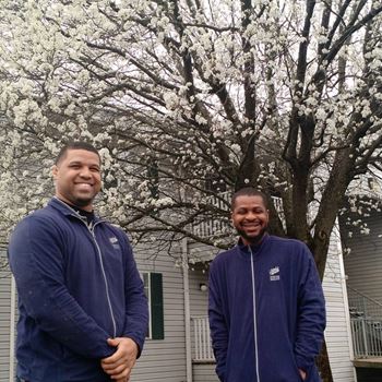 Two men in blue jackets standing in front of a tree with white flowers.